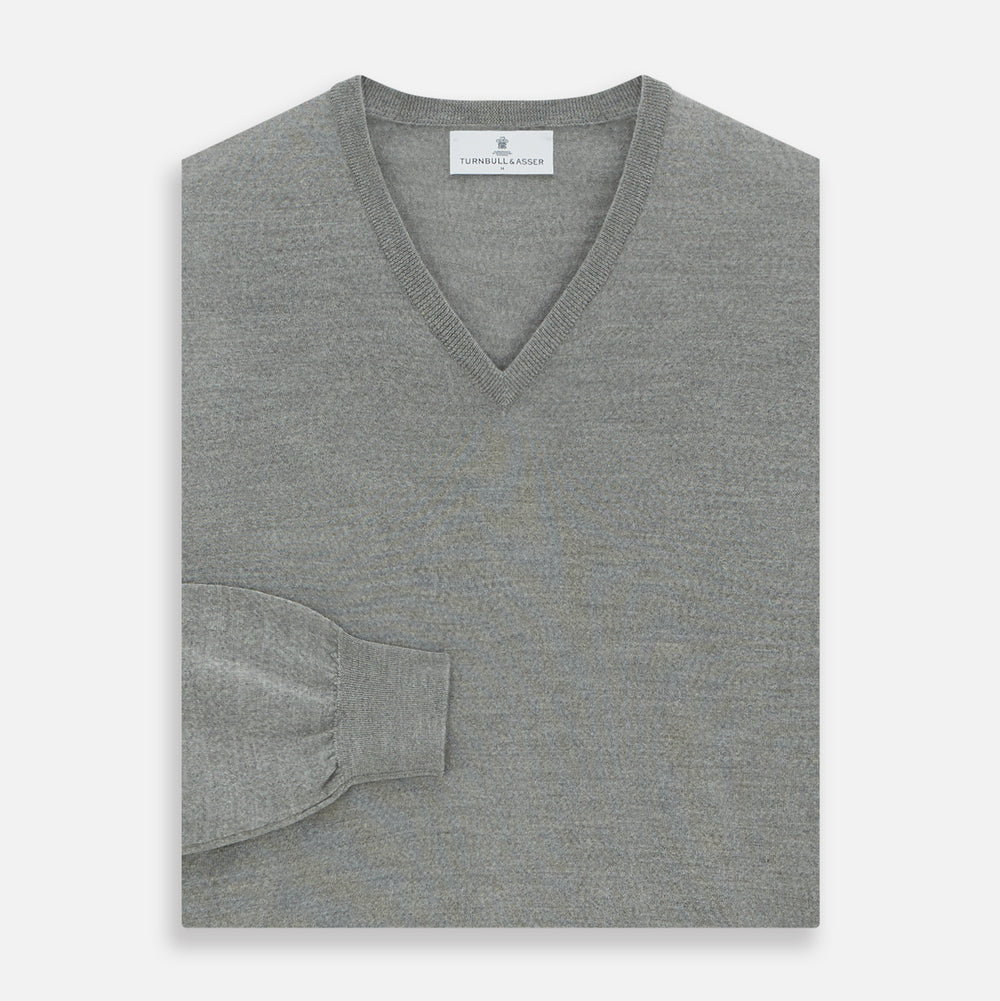 The Grey V-Neck Merino Wool Jumper by Turnbull & Asser features long sleeves with ribbed cuffs and hem, making it a versatile wardrobe essential for any gentleman. Shown here in classic light grey on a white background.