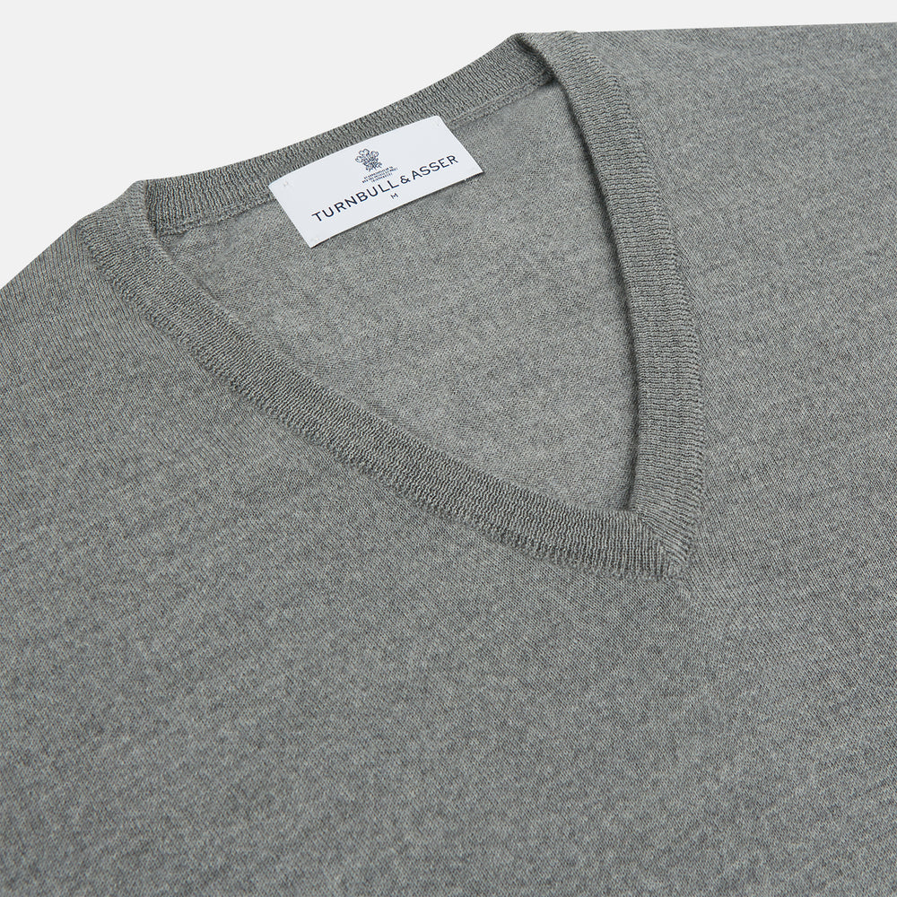 The Grey V-Neck Merino Wool Jumper by Turnbull & Asser features long sleeves with ribbed cuffs and hem, making it a versatile wardrobe essential for any gentleman. Shown here in classic light grey on a white background.
