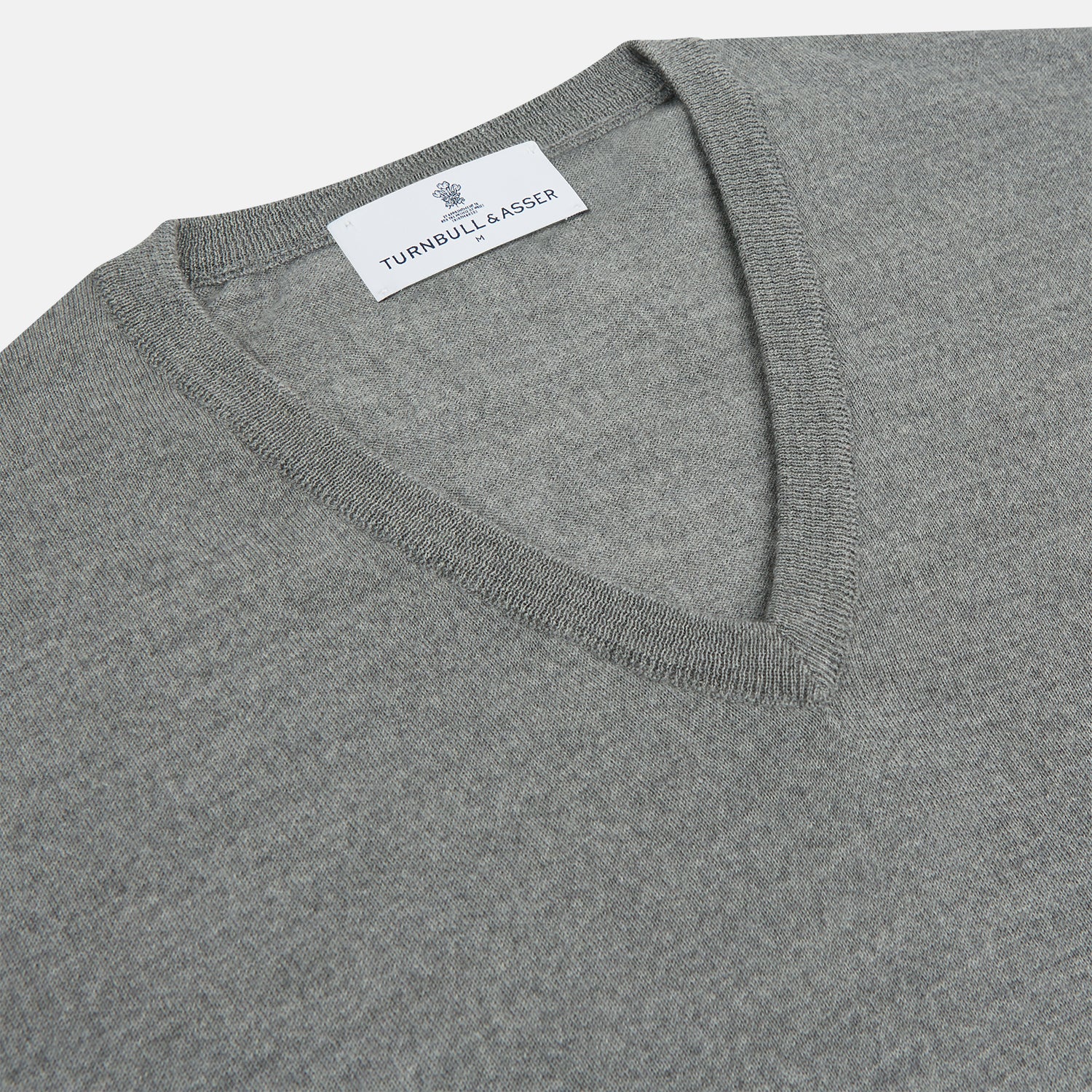 View 2 of product The Grey V-Neck Merino Wool Jumper by Turnbull & Asser features long sleeves with ribbed cuffs and hem, making it a versatile wardrobe essential for any gentleman. Shown here in classic light grey on a white background.