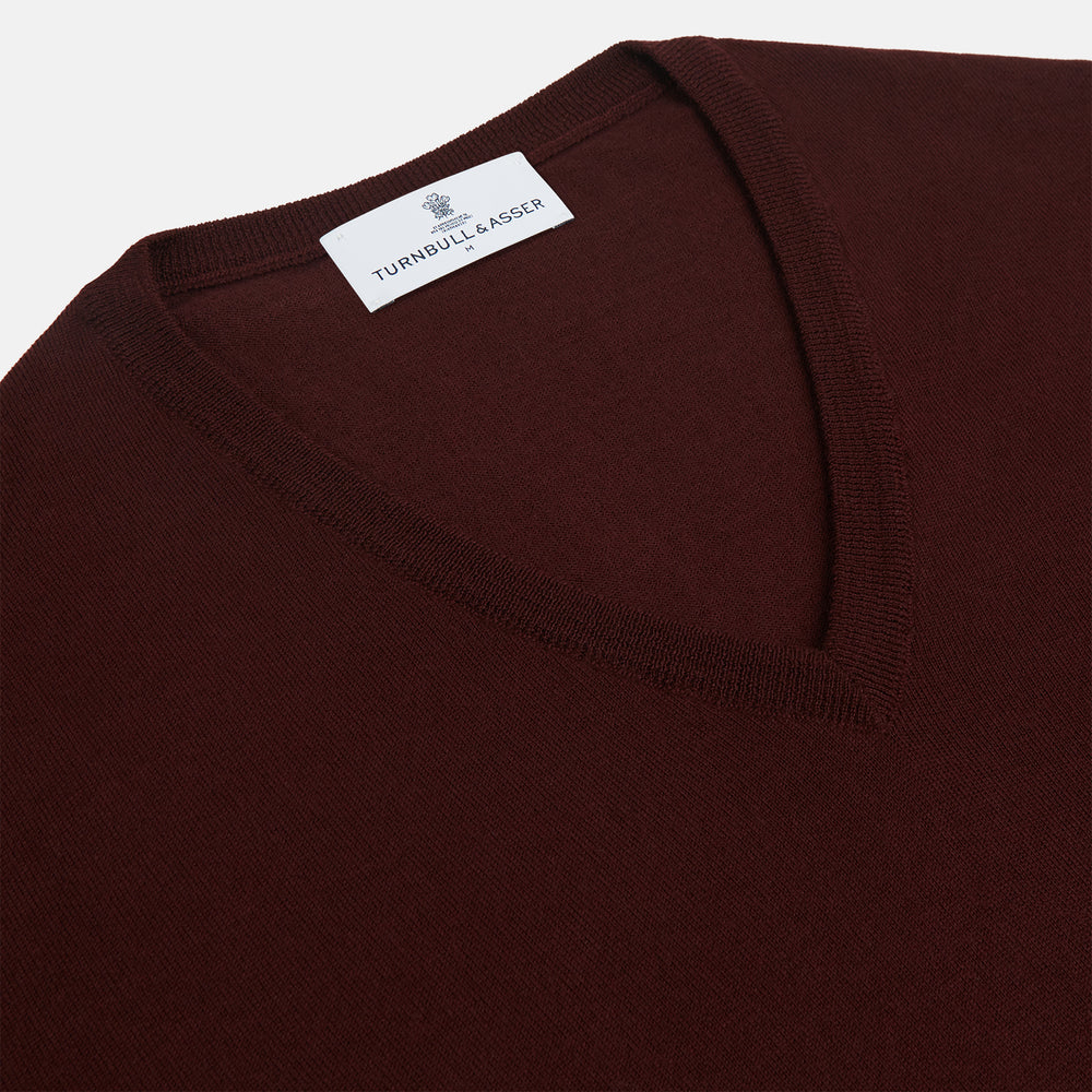 The Turnbull & Asser Wine V-Neck Merino Wool Jumper features long sleeves and ribbed cuffs and waistband, shown flat on a white background—a timeless staple for any gentleman’s wardrobe.