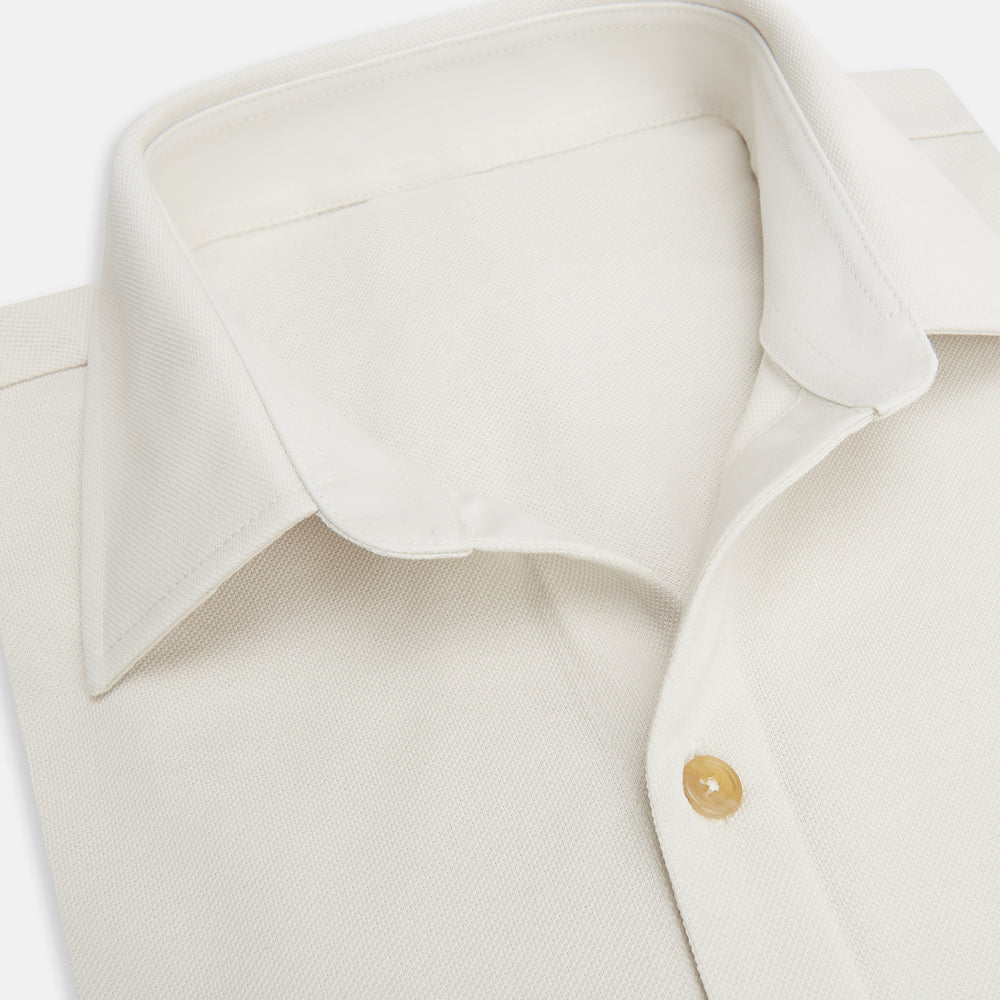 The Turnbull & Asser White Pique Shirt is a long-sleeve, white button-up with a chest pocket and beige buttons, laid flat on a white background, featuring an elevated silhouette inspired by elegant polos.