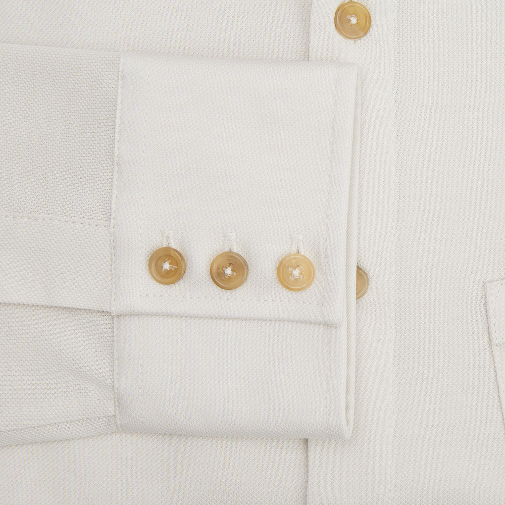 The Turnbull & Asser White Pique Shirt is a long-sleeve, white button-up with a chest pocket and beige buttons, laid flat on a white background, featuring an elevated silhouette inspired by elegant polos.