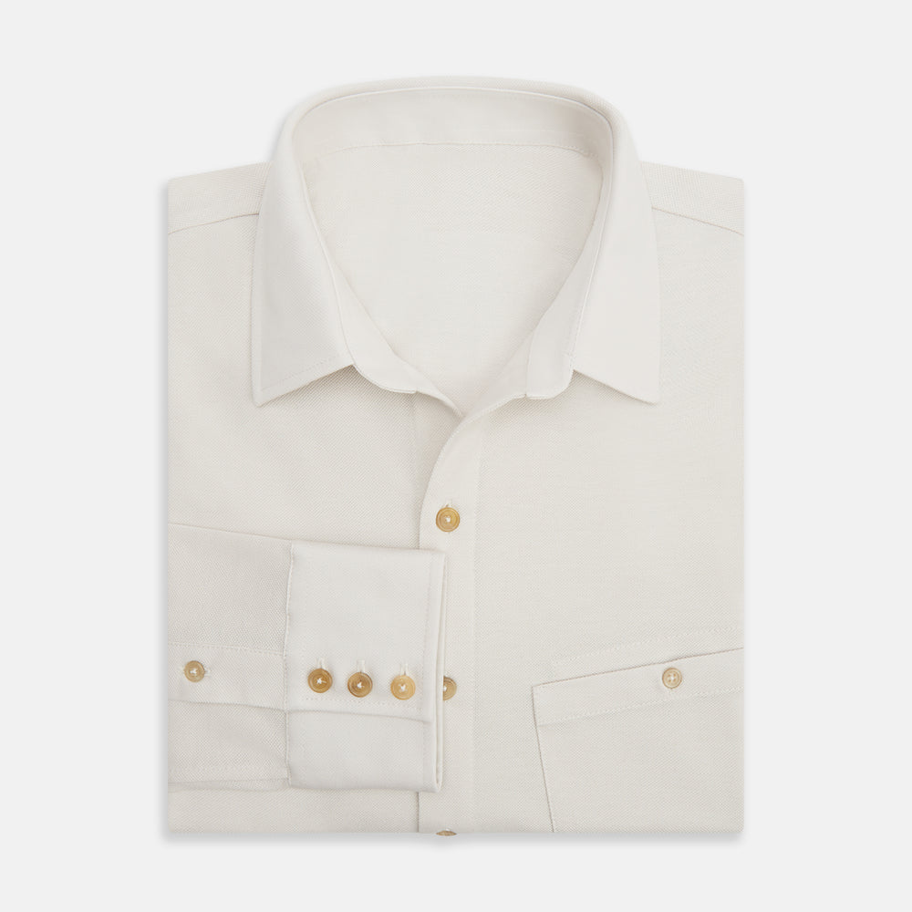 The Turnbull & Asser White Pique Shirt is a long-sleeve, white button-up with a chest pocket and beige buttons, laid flat on a white background, featuring an elevated silhouette inspired by elegant polos.