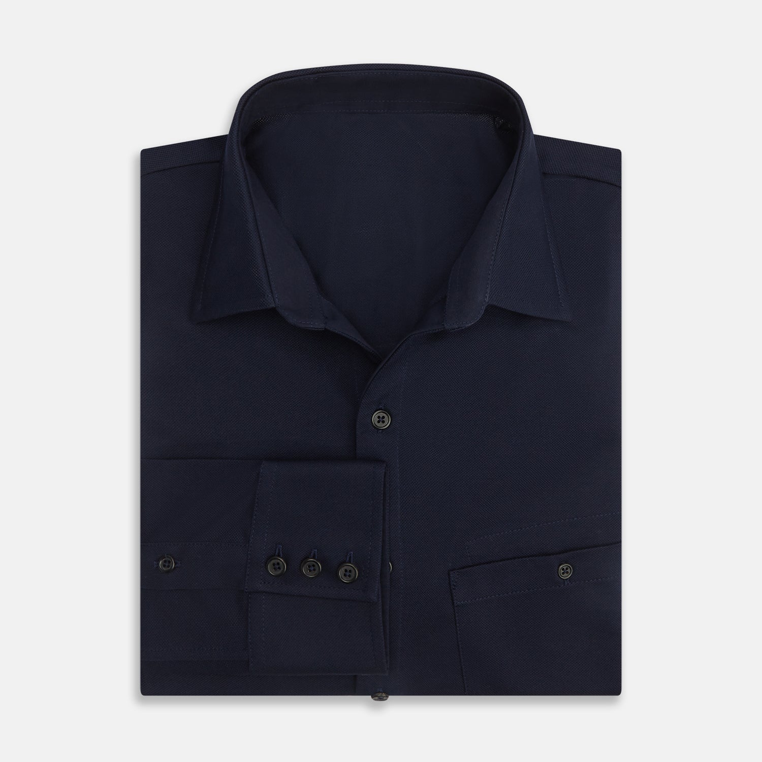 View 5 of product The Turnbull & Asser Navy Pique Shirt is a long-sleeved, dark navy button-up with a left chest pocket, classic collar, and buttoned cuffs, shown laid flat on a white background.