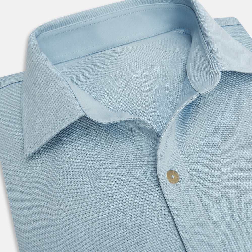 The Turnbull & Asser Pale Blue Pique Shirt is a long-sleeve button-up with an open collar, single chest pocket, and beige buttons, shown against a white background.