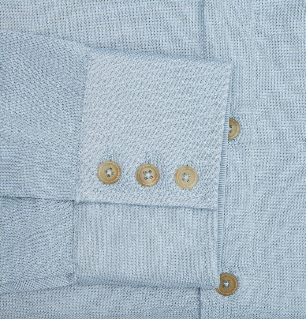 The Turnbull & Asser Pale Blue Pique Shirt is a long-sleeve button-up with an open collar, single chest pocket, and beige buttons, shown against a white background.
