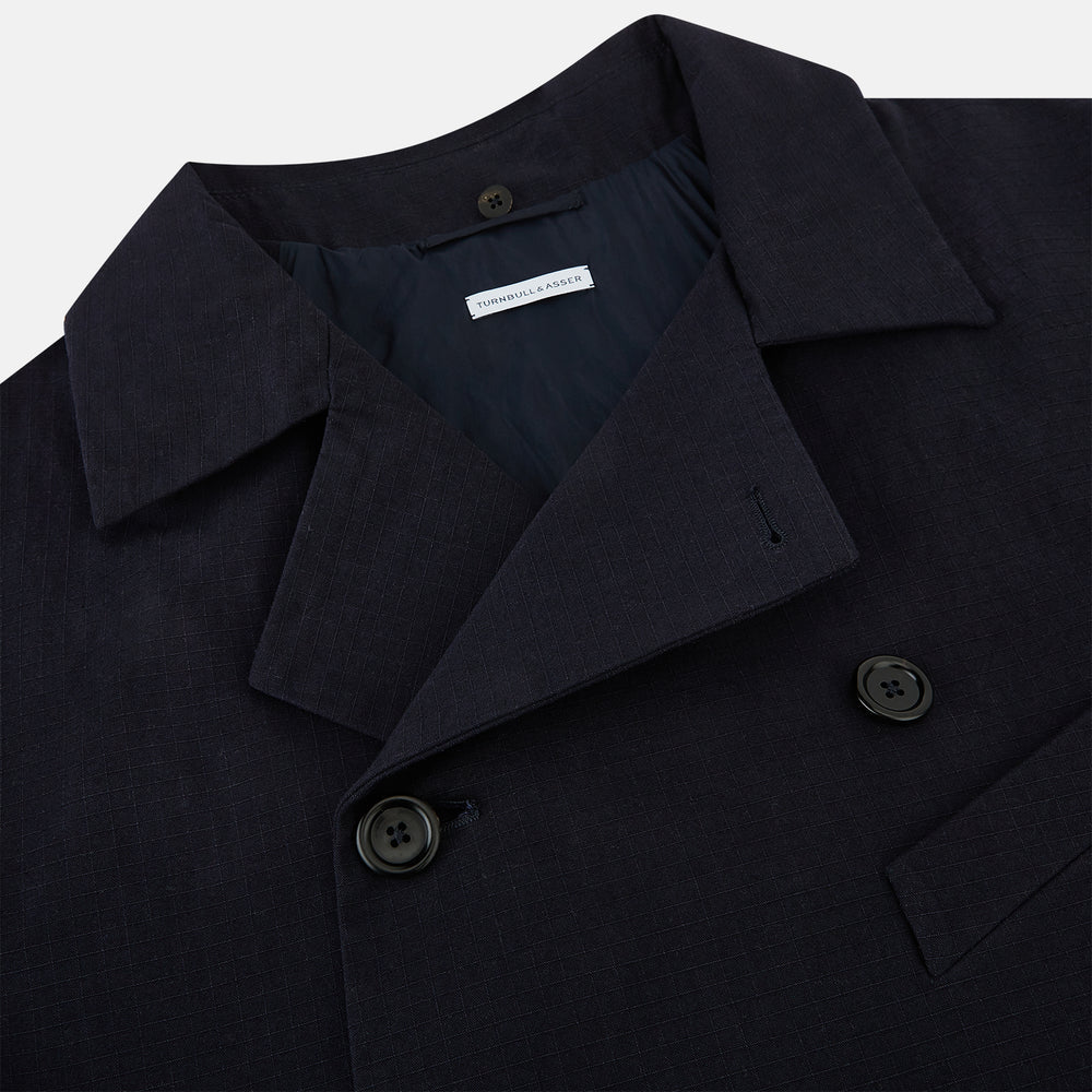 The Navy Short Albert Trench Coat by Turnbull & Asser UK features dark navy fabric, six black buttons, a notched collar, long sleeves with adjustable cuffs, and front zip pockets—displayed on a plain white background.