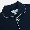 View 2 of product The Turnbull & Asser Navy Piped Cotton Pyjama Set features a navy blue long-sleeve top with white piping, front buttons, a chest pocket, and matching drawstring pants, all displayed on a white background.