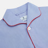 View 2 of product The Blue Piped End-on-End Cotton Pyjama Set by Turnbull & Asser features light blue long sleeves, red piping, front buttons, chest pocket, and matching drawstring pants—luxurious sleepwear laid flat on a white background.