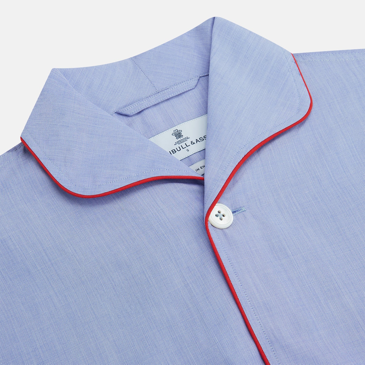 View 2 of product The Blue Piped End-on-End Cotton Pyjama Set by Turnbull & Asser features light blue long sleeves, red piping, front buttons, chest pocket, and matching drawstring pants—luxurious sleepwear laid flat on a white background.