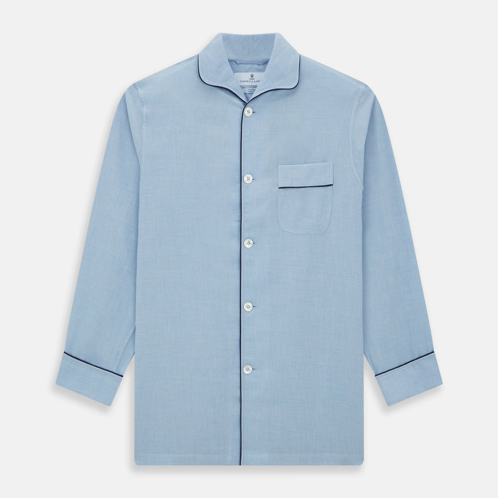 The Blue Piped Cotton-Cashmere Pyjama Set by Turnbull & Asser features a light blue long-sleeved, button-up top with a chest pocket and dark piping, plus matching side-tie pants—luxurious comfort displayed on a white background.