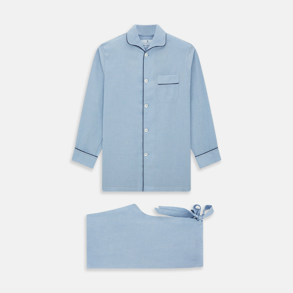 The Blue Piped Cotton-Cashmere Pyjama Set by Turnbull & Asser features a light blue long-sleeved, button-up top with a chest pocket and dark piping, plus matching side-tie pants—luxurious comfort displayed on a white background.