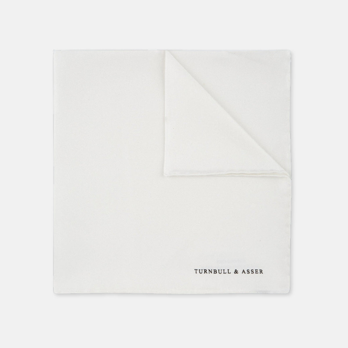 View 1 of product The White Piped Silk Pocket Square by Turnbull & Asser is shown folded at one corner with the brand's logo in black on the lower right, set against a light blue background.