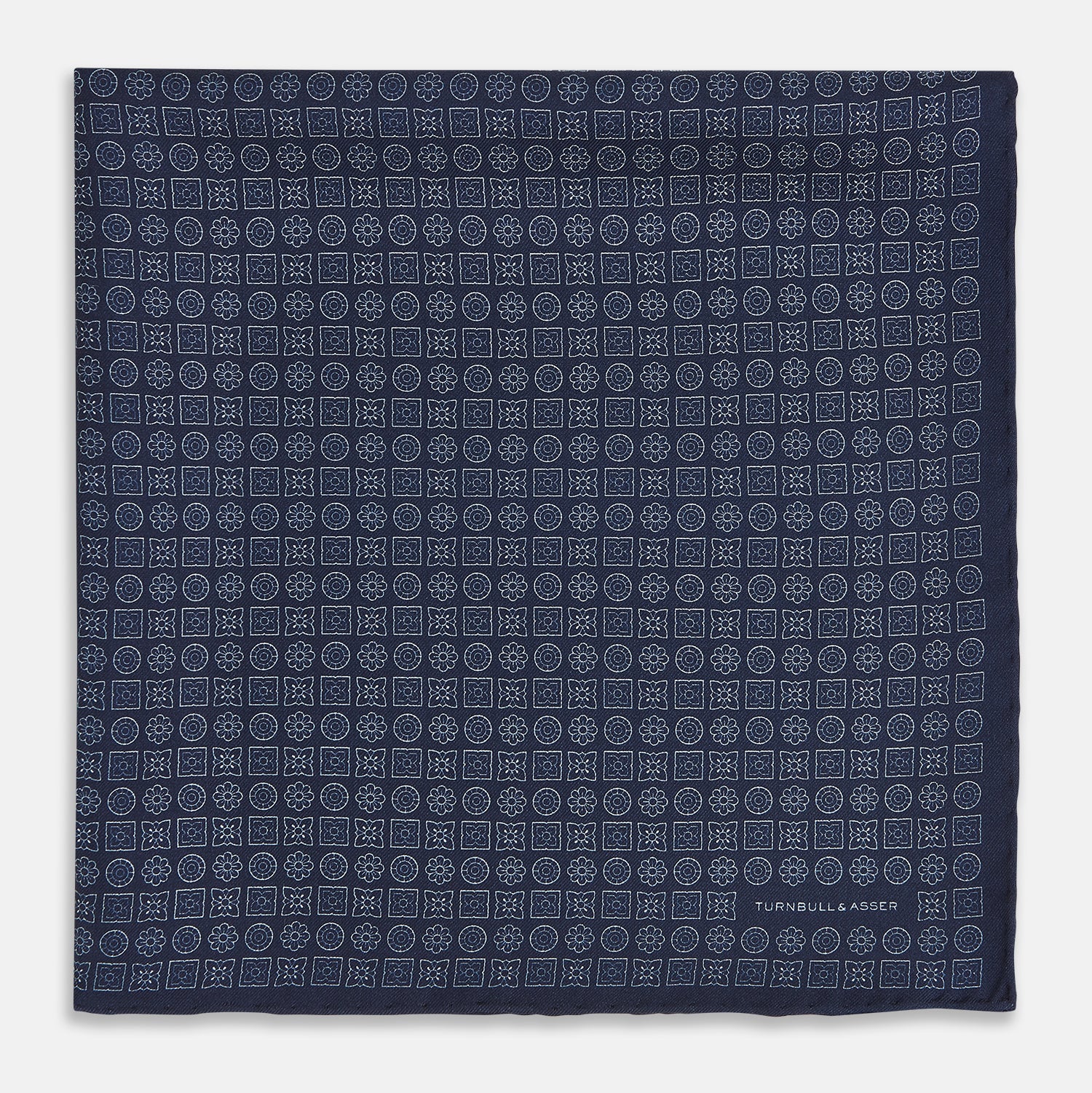 View 3 of product A Floral Navy Pocket Square in Silk by Turnbull & Asser UK, featuring a repeating geometric pattern with the brand’s name printed in white in the corner—perfect for adding a touch of sophistication to formal tailoring. The top right edge is folded over to reveal the reverse side.