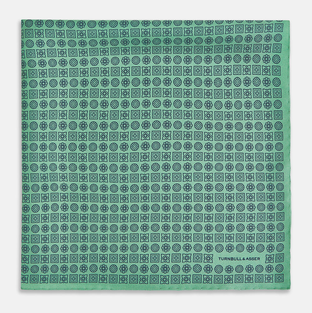 Floral Green Pocket Square in Silk by Turnbull & Asser UK, showcasing navy-blue floral geometric motifs on a bright green background. One corner is neatly folded to display both sides of the silk fabric, with "Turnbull & Asser UK" printed in the lower right corner.