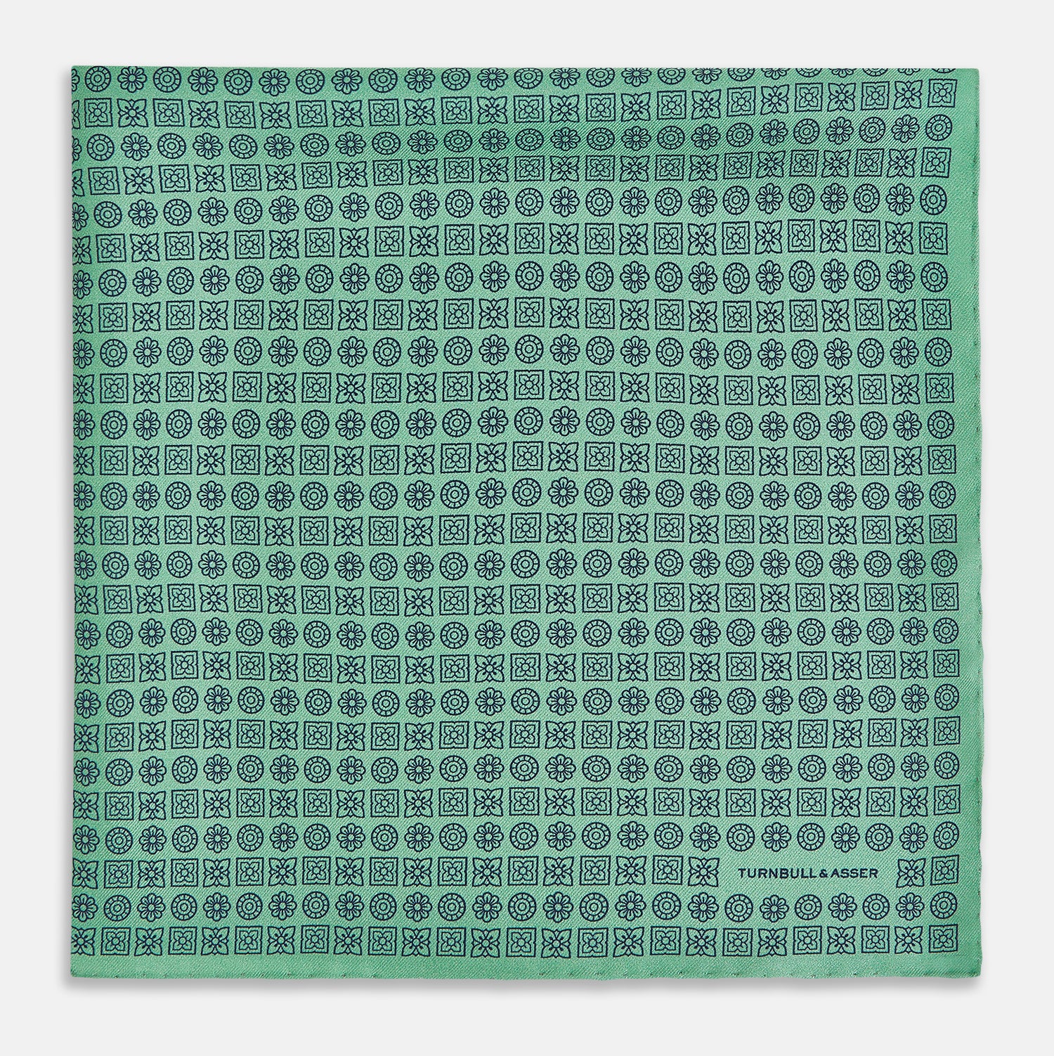 View 3 of product Floral Green Pocket Square in Silk by Turnbull & Asser UK, showcasing navy-blue floral geometric motifs on a bright green background. One corner is neatly folded to display both sides of the silk fabric, with "Turnbull & Asser UK" printed in the lower right corner.