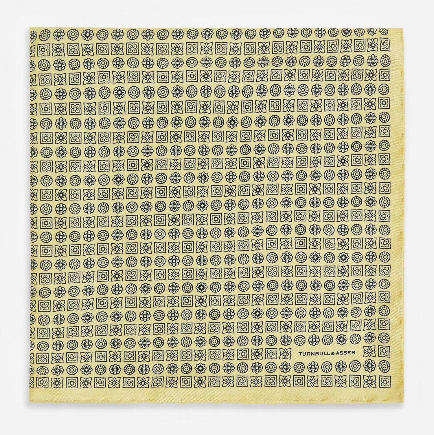 View 3 of product A Floral Yellow Pocket Square in Silk by Turnbull & Asser UK, showcasing a repeating black geometric pattern with subtle floral motifs and the brand logo in one corner. One corner of the fabric is folded over to display the reverse side.