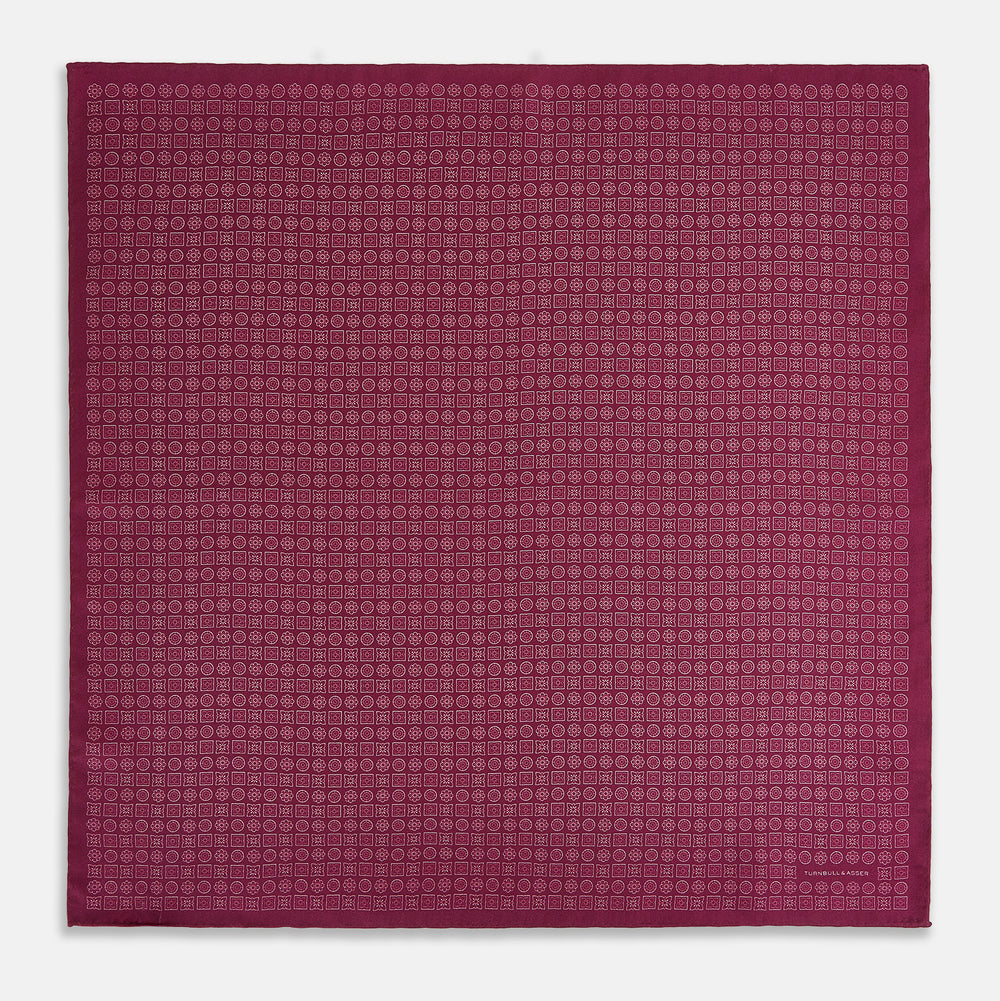 A folded Floral Burgundy Pocket Square in Silk by Turnbull & Asser UK, adorned with pink floral geometric motifs and featuring the Turnbull & Asser logo in the bottom right corner.