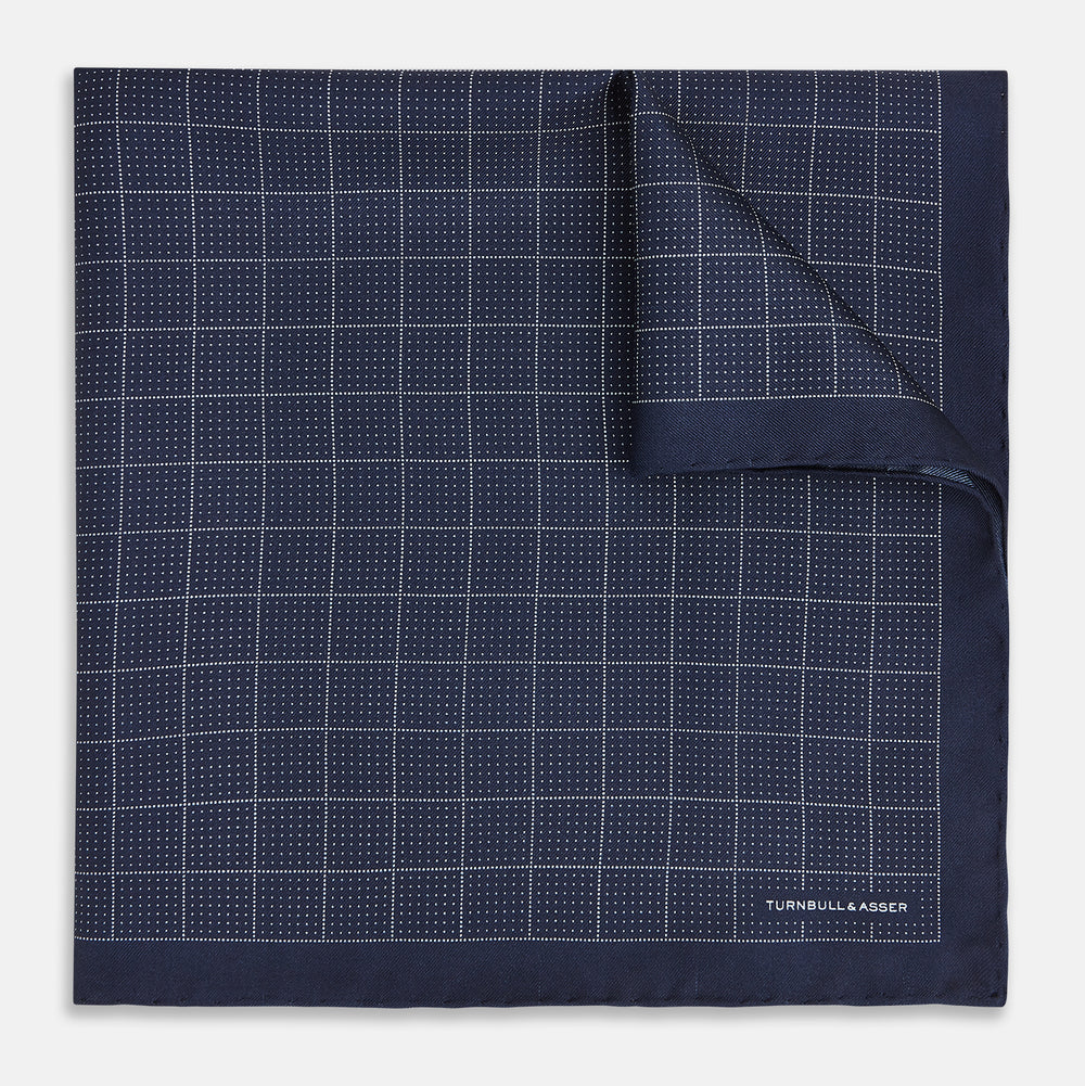 Checked Navy On White Pocket Square in Silk by Turnbull & Asser UK, featuring a navy blue geometric pattern with a white dotted grid and a solid border. The pocket square is shown with one corner folded over to display the “TURNBULL & ASSER” label in white text.