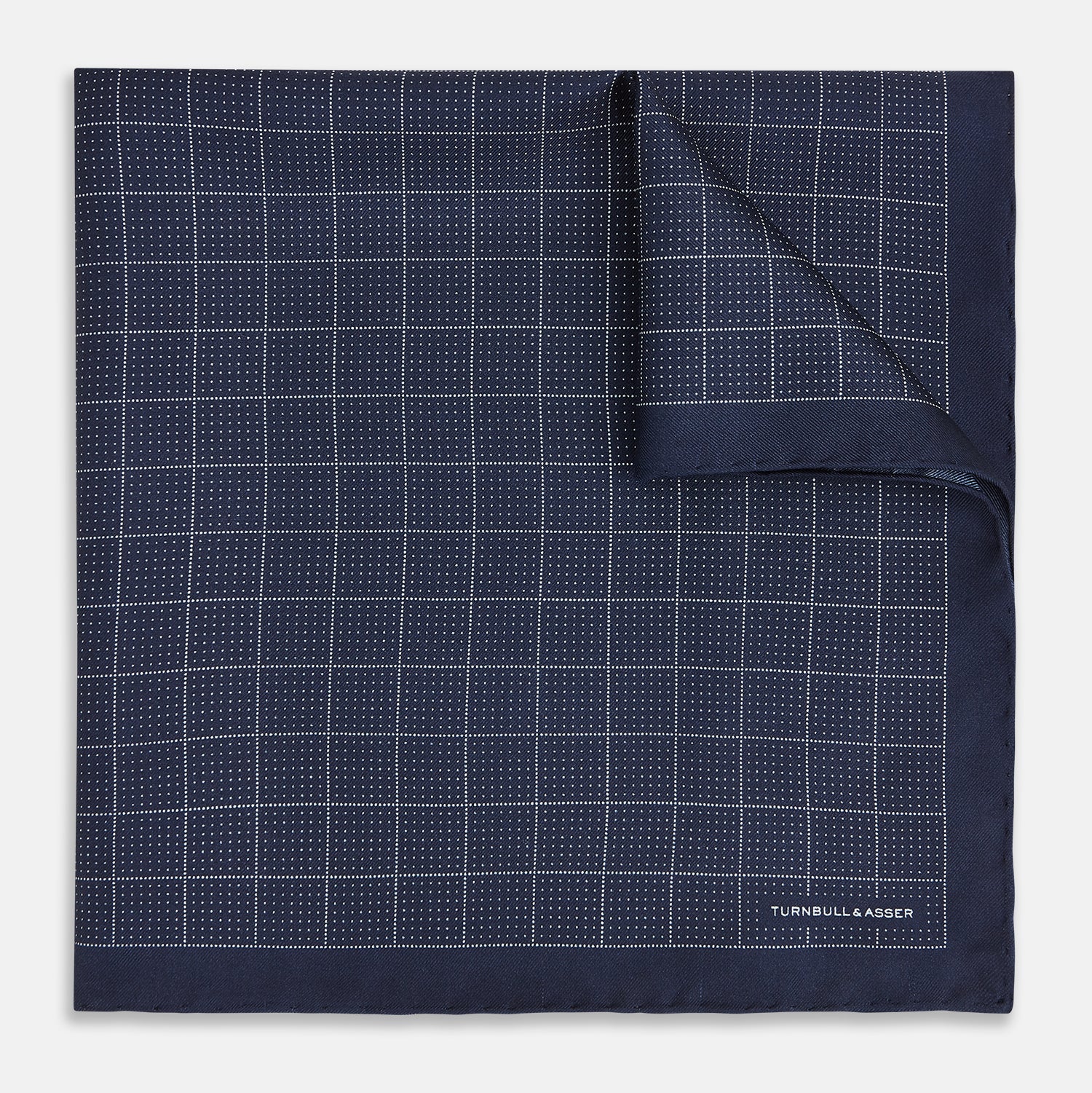View 1 of product Checked Navy On White Pocket Square in Silk by Turnbull & Asser UK, featuring a navy blue geometric pattern with a white dotted grid and a solid border. The pocket square is shown with one corner folded over to display the “TURNBULL & ASSER” label in white text.