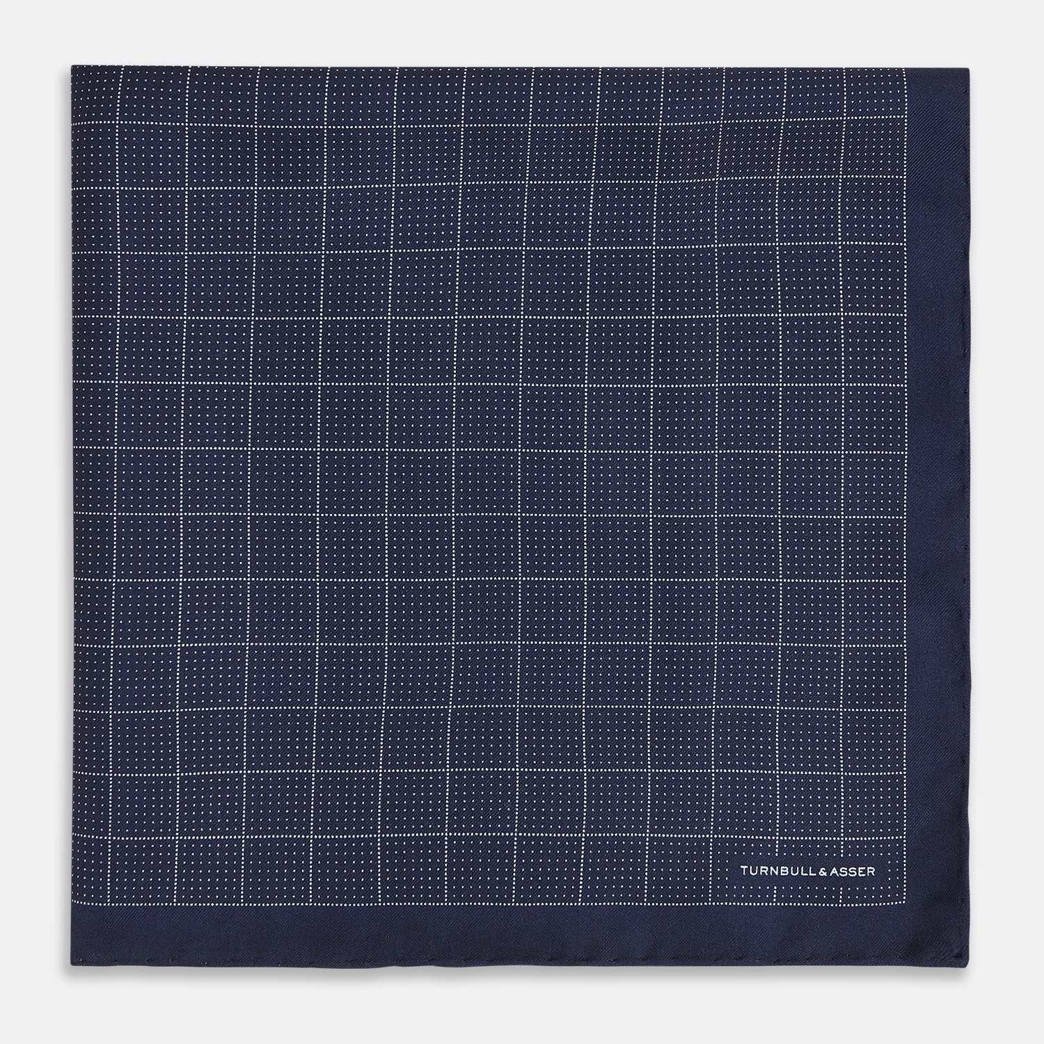View 3 of product Checked Navy On White Pocket Square in Silk by Turnbull & Asser UK, featuring a navy blue geometric pattern with a white dotted grid and a solid border. The pocket square is shown with one corner folded over to display the “TURNBULL & ASSER” label in white text.