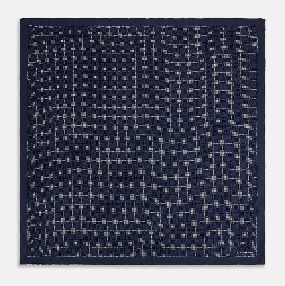 Checked Navy On White Pocket Square in Silk by Turnbull & Asser UK, featuring a navy blue geometric pattern with a white dotted grid and a solid border. The pocket square is shown with one corner folded over to display the “TURNBULL & ASSER” label in white text.