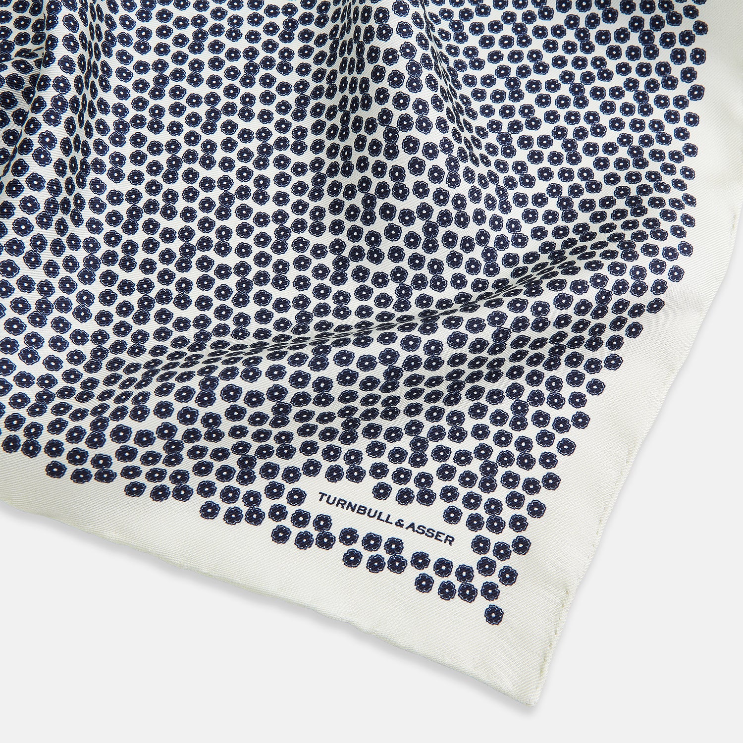 View 2 of product A refined double-sided design, the Floral White Pocket Square in Silk by Turnbull & Asser UK features a small blue floral pattern on white silk, neatly folded to display both its intricate front and bordered corner—adding subtle elegance to any ensemble.