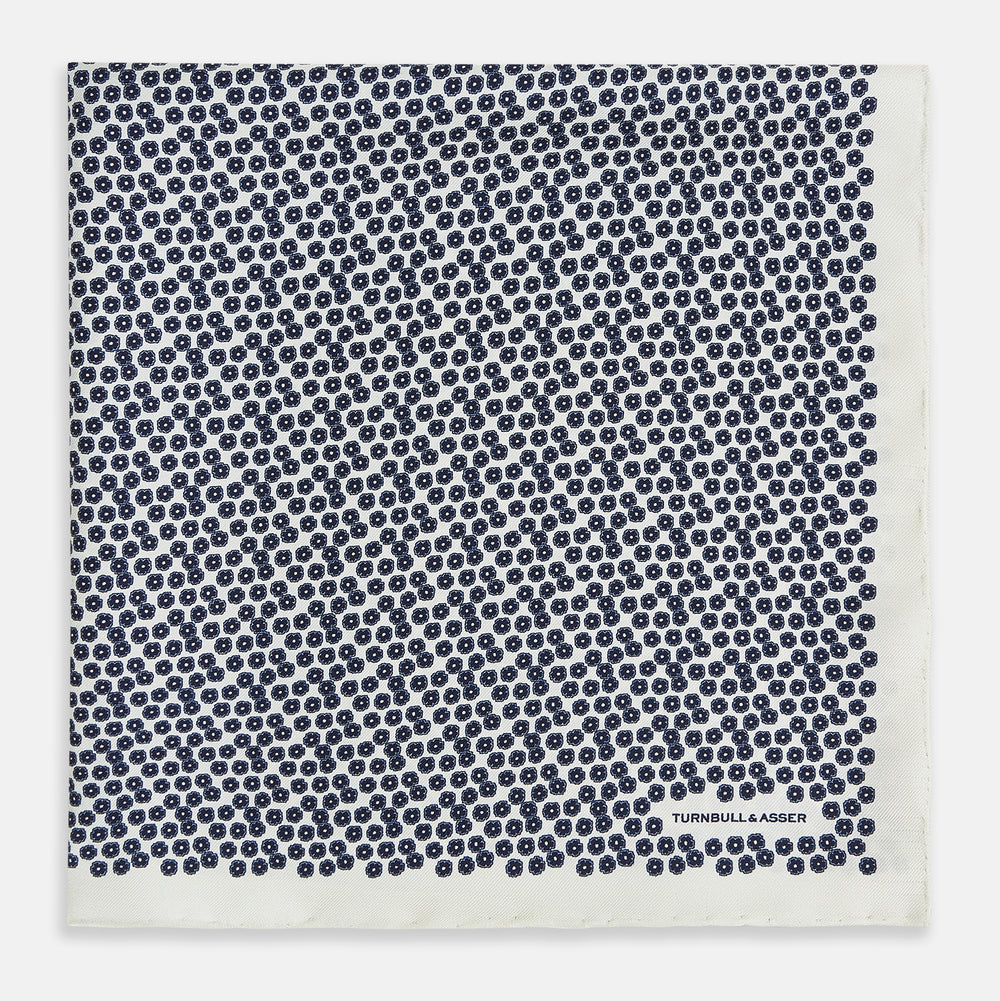 A refined double-sided design, the Floral White Pocket Square in Silk by Turnbull & Asser UK features a small blue floral pattern on white silk, neatly folded to display both its intricate front and bordered corner—adding subtle elegance to any ensemble.