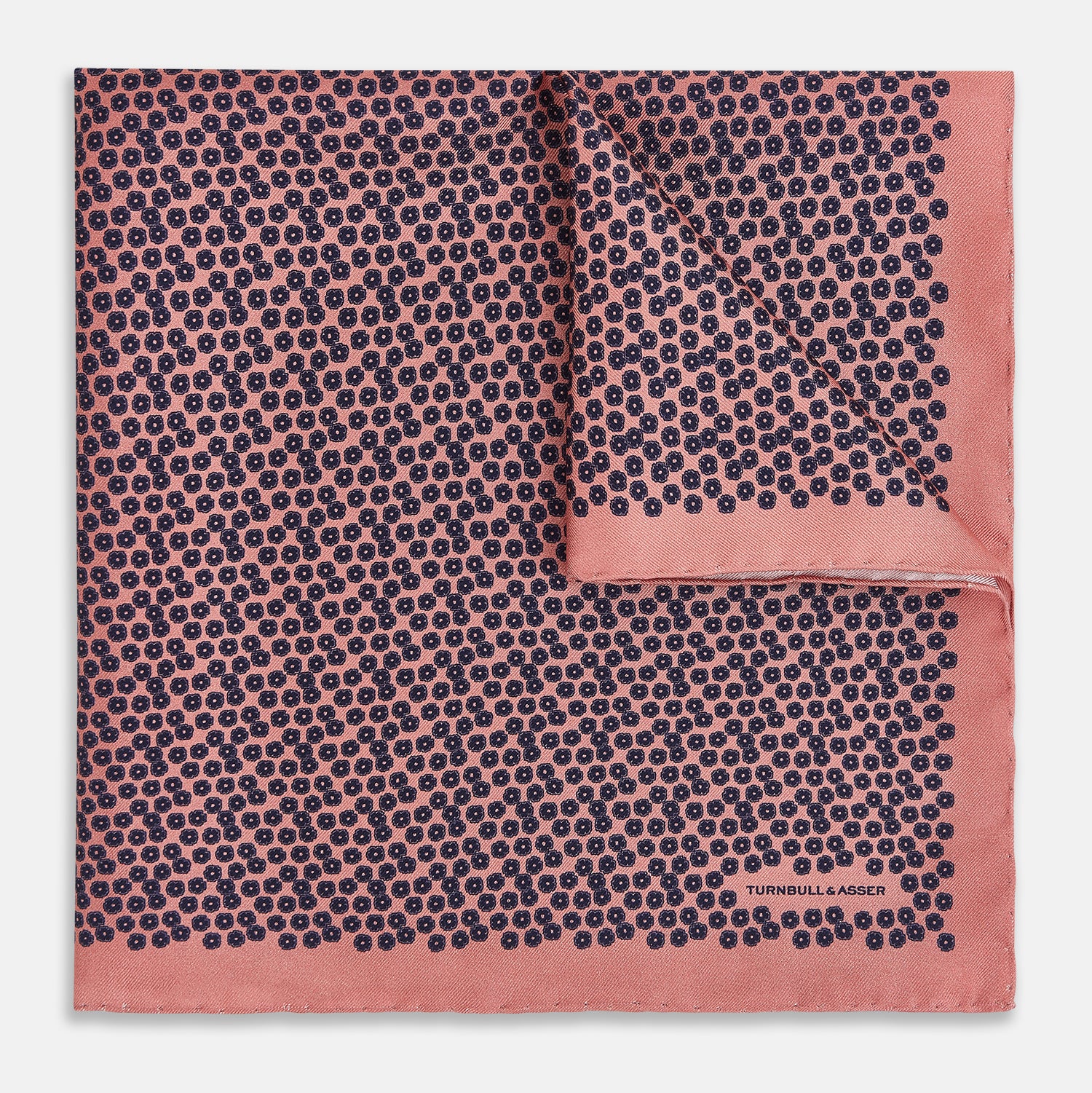 View 1 of product A folded Floral Pink Pocket Square in Silk by Turnbull & Asser UK, adorned with a pattern of small navy blue circles and the brand name printed in one corner, features a refined double-sided design for added versatility.