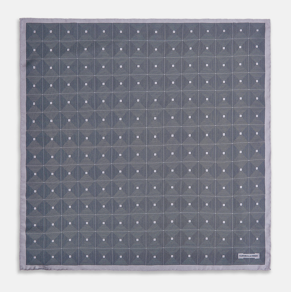 A folded, square Turnbull & Asser UK Geometric Grey Pocket Square in Silk featuring a geometric black and white concentric squares pattern accented with subtle navy lines, finished with a small Turnbull & Asser label in one corner.