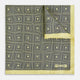 A checked yellow silk pocket square from Turnbull & Asser UK, featuring black and white concentric square designs with a yellow border. It is partially folded to highlight its double-sided pattern, and a small label reading TURNBULL & ASSER is visible in one corner.