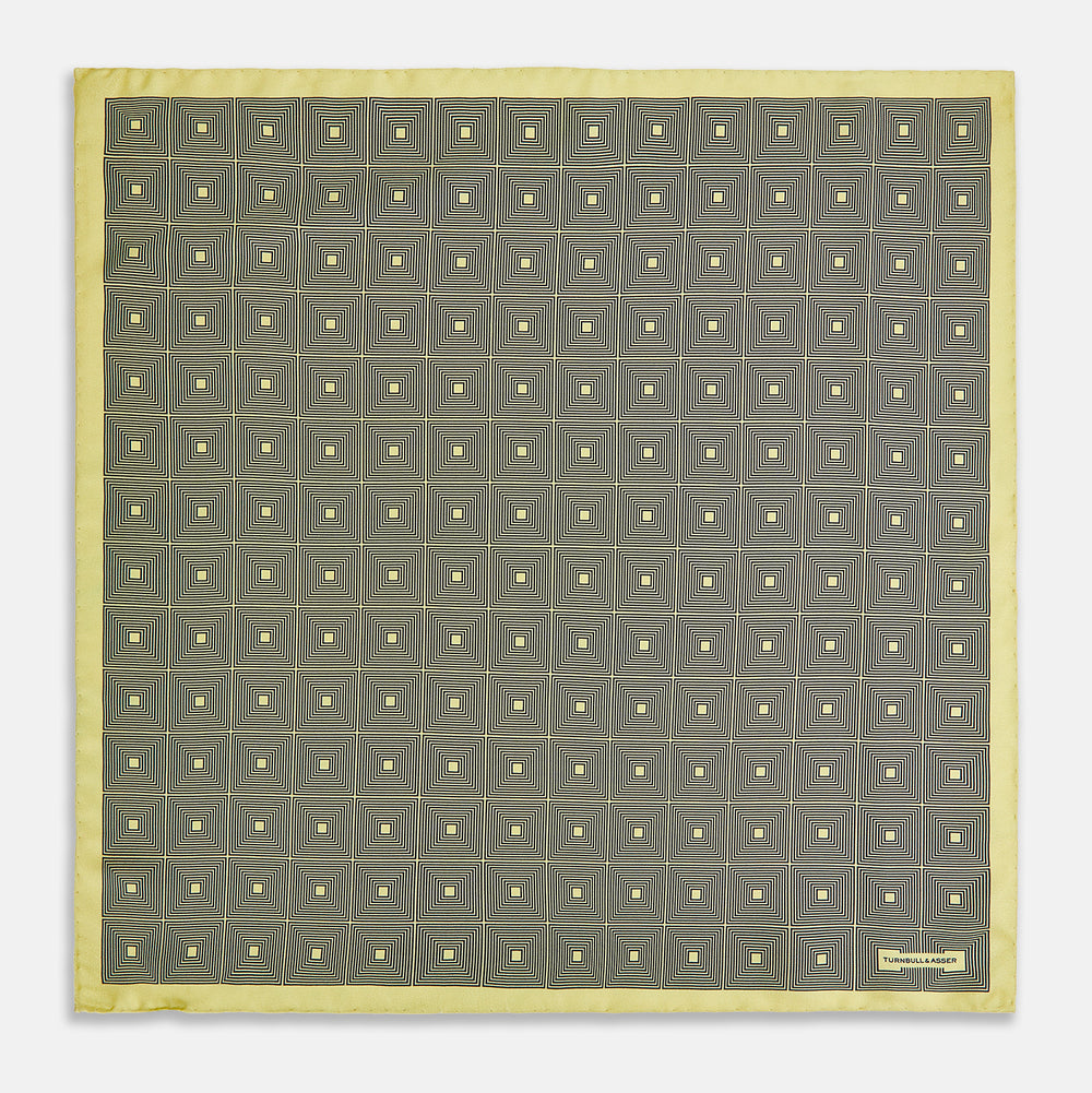 A checked yellow silk pocket square from Turnbull & Asser UK, featuring black and white concentric square designs with a yellow border. It is partially folded to highlight its double-sided pattern, and a small label reading TURNBULL & ASSER is visible in one corner.