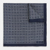View 1 of product A Geometric Navy Pocket Square in Silk by Turnbull & Asser UK, showcasing a geometric pattern of small, overlapping concentric white squares and a stitched border. The pocket square is pictured with one corner folded over to display the Turnbull & Asser UK brand label.