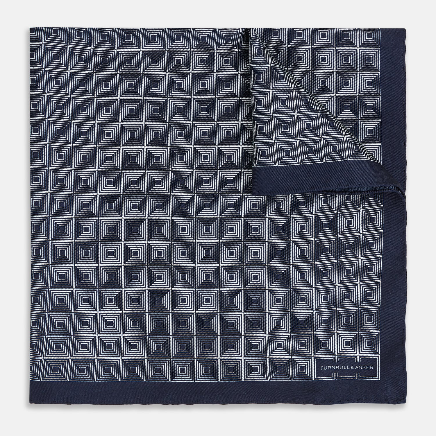 View 1 of product A Geometric Navy Pocket Square in Silk by Turnbull & Asser UK, showcasing a geometric pattern of small, overlapping concentric white squares and a stitched border. The pocket square is pictured with one corner folded over to display the Turnbull & Asser UK brand label.