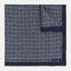 A Geometric Navy Pocket Square in Silk by Turnbull & Asser UK, showcasing a geometric pattern of small, overlapping concentric white squares and a stitched border. The pocket square is pictured with one corner folded over to display the Turnbull & Asser UK brand label.