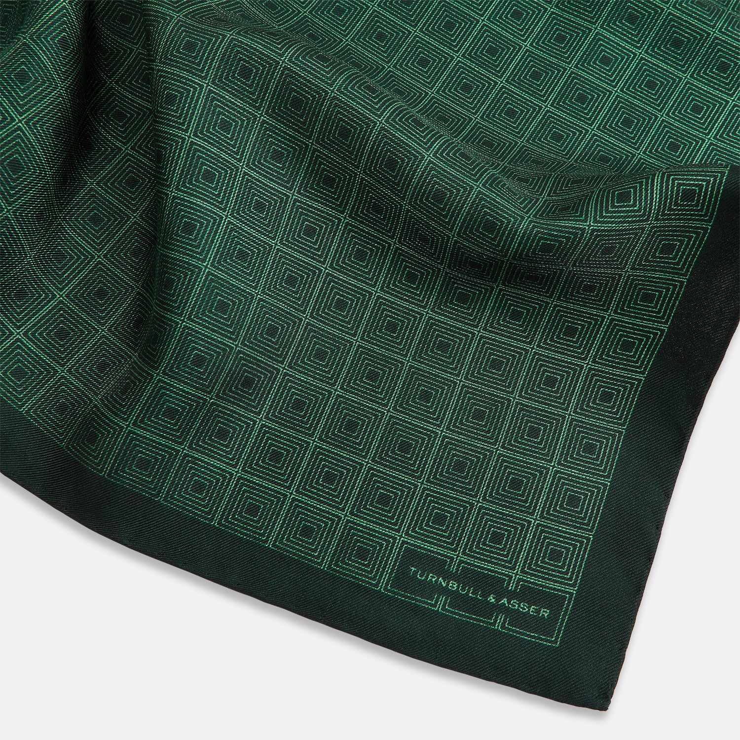 View 2 of product The Geometric Green Pocket Square in Silk by Turnbull & Asser UK features a sophisticated forest green hue with a geometric pattern of concentric squares and a visible Turnbull & Asser label in the corner.