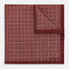 View 1 of product The Geometric Burgundy Pocket Square in Silk by Turnbull & Asser UK features a refined pattern of small, repeating white squares on a rich burgundy background—an ideal accessory for introducing sophistication to any outfit. One corner is artfully folded over to showcase the reverse side of this elegant geometric design, and the "Turnbull & Asser" label appears in the bottom right corner.