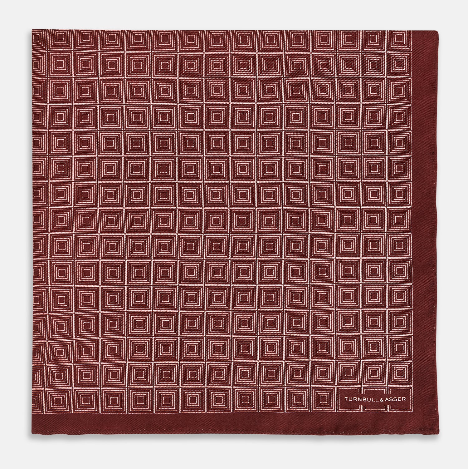 View 3 of product The Geometric Burgundy Pocket Square in Silk by Turnbull & Asser UK features a refined pattern of small, repeating white squares on a rich burgundy background—an ideal accessory for introducing sophistication to any outfit. One corner is artfully folded over to showcase the reverse side of this elegant geometric design, and the "Turnbull & Asser" label appears in the bottom right corner.