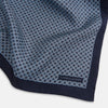 View 2 of product Introducing the Geometric Navy Pocket Square in Silk by Turnbull & Asser UK. This sophisticated accessory showcases a small, repeating geometric pattern in light blue and white on a rich navy background. The pocket square features a solid navy border, while the folded corner reveals the underside adorned with the Turnbull & Asser logo—an elegant finishing touch for any formal ensemble.