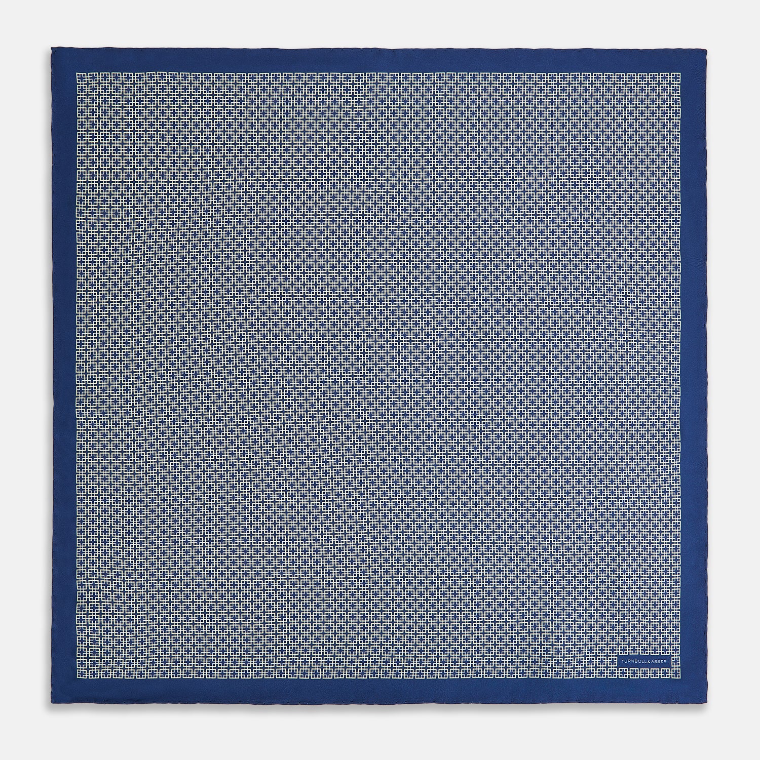 View 4 of product A blue pocket square from Turnbull & Asser UK, featuring a geometric white square pattern and a solid blue border. One corner is folded to highlight the striking design on both sides, with the brand name displayed on the bottom right. Product name: POCKET SQUARE SQUARE PATTERNED BANANA.