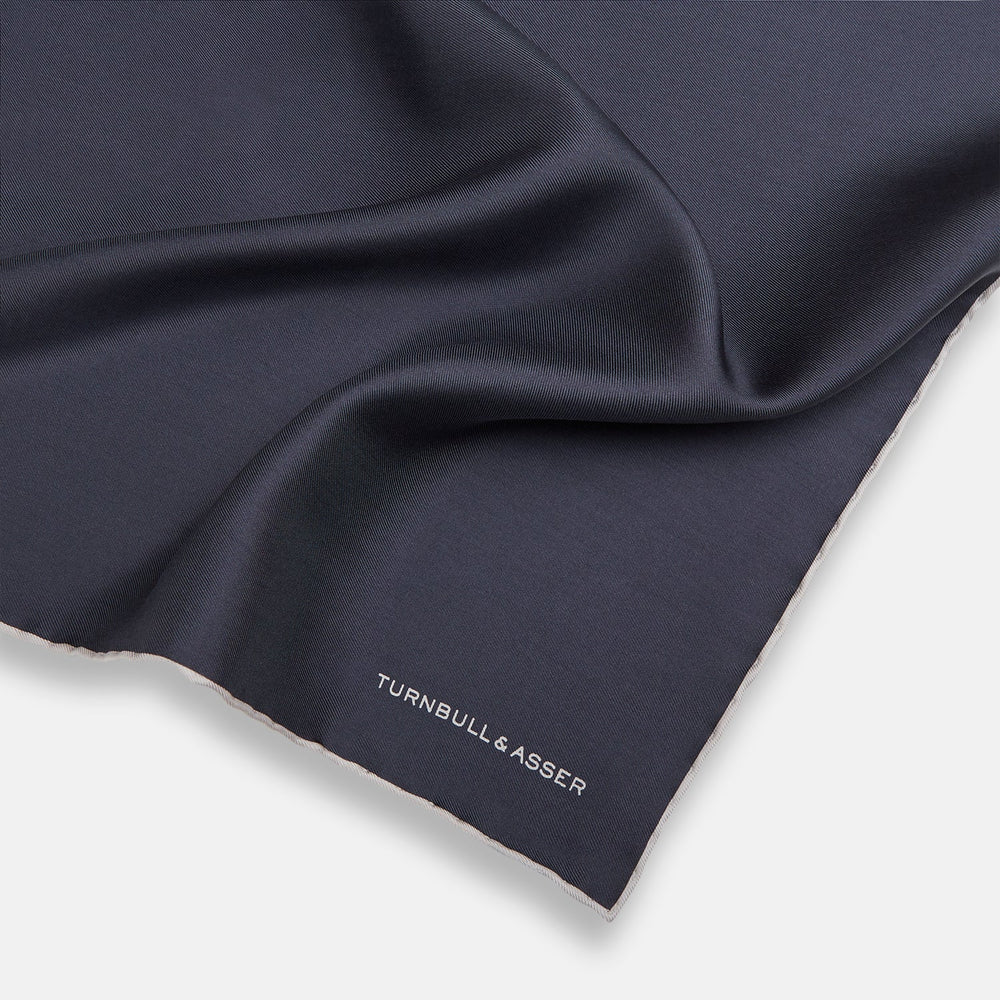 A neatly folded grey silk pocket square with ecru piping—ideal for formal wear—and TURNBULL & ASSER printed in white in one corner.