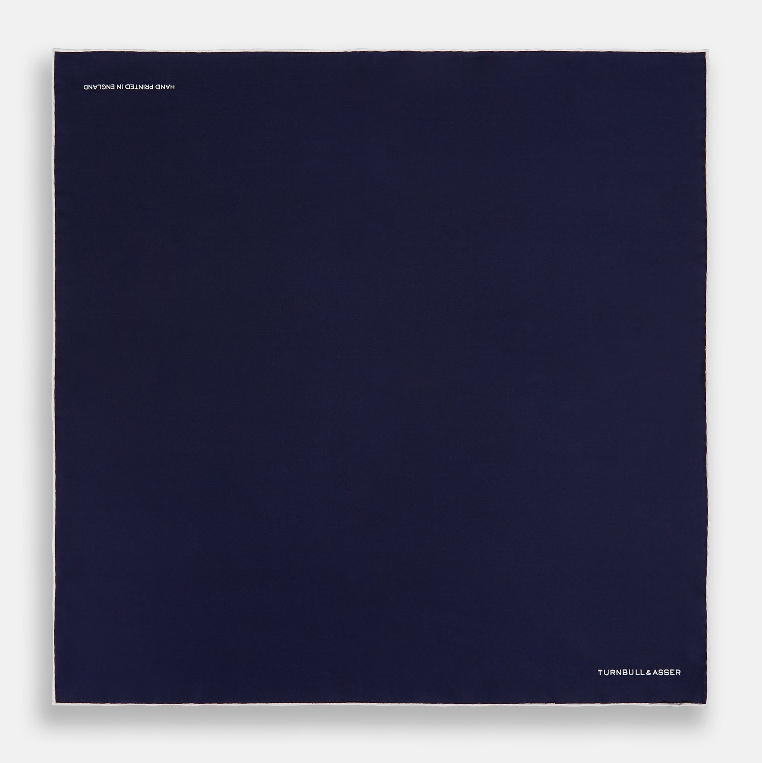 View 4 of product The Navy Piped Silk Pocket Square by Turnbull & Asser features white-stitched edges and subtle brand embroidery, ideal for enhancing formal looks. Shown neatly folded on a plain white background.