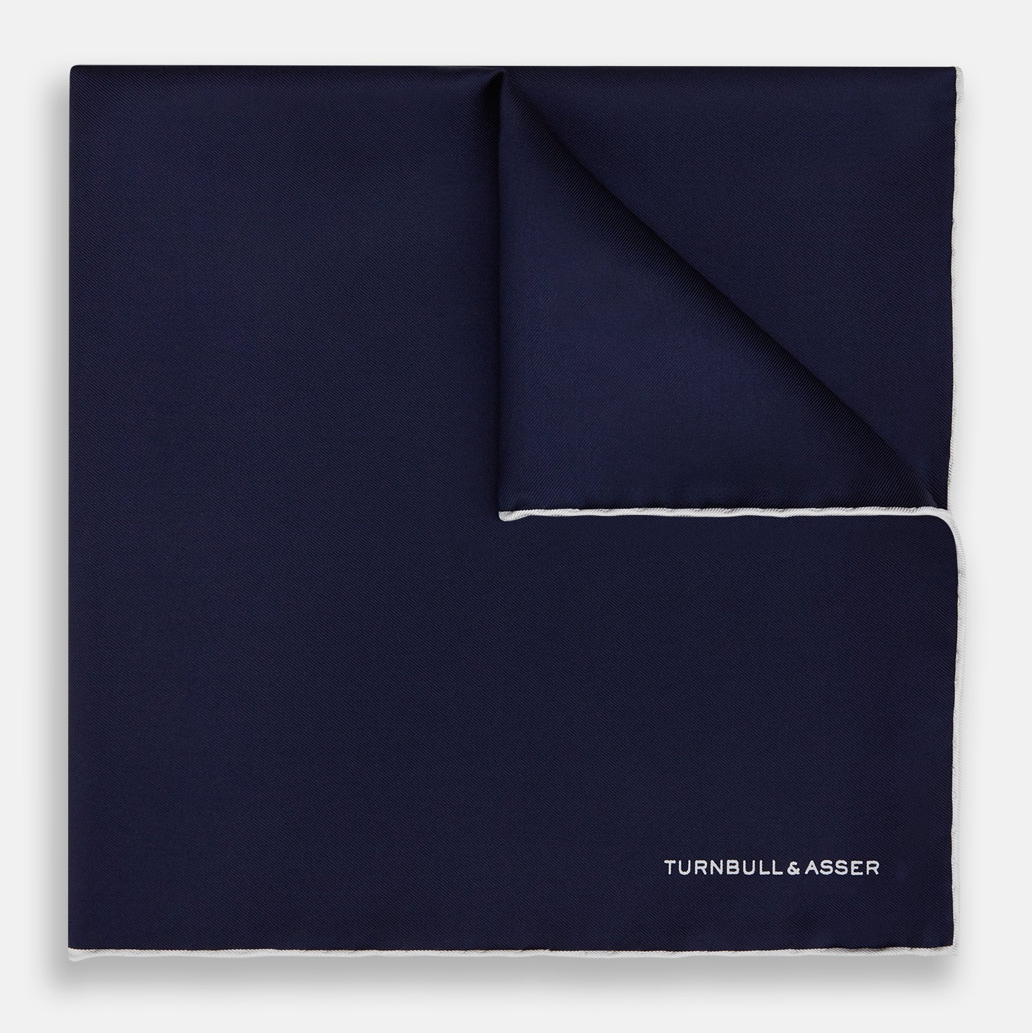View 1 of product The Navy Piped Silk Pocket Square by Turnbull & Asser features white-stitched edges and subtle brand embroidery, ideal for enhancing formal looks. Shown neatly folded on a plain white background.