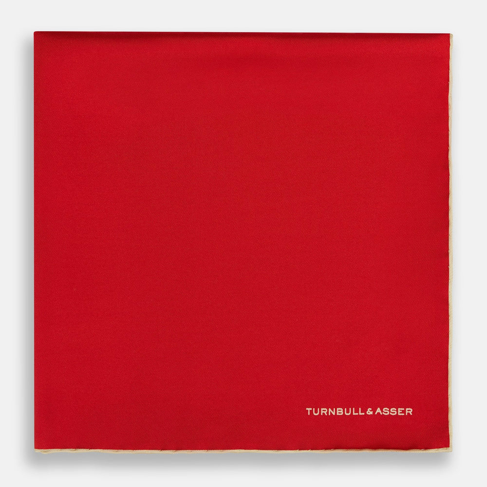 The Turnbull & Asser RED AND GOLD PIPED SILK POCKET SQUARE is a vibrant red silk accessory with gold edging and the brand’s logo in white on the bottom right—ideal for elevating formal looks.