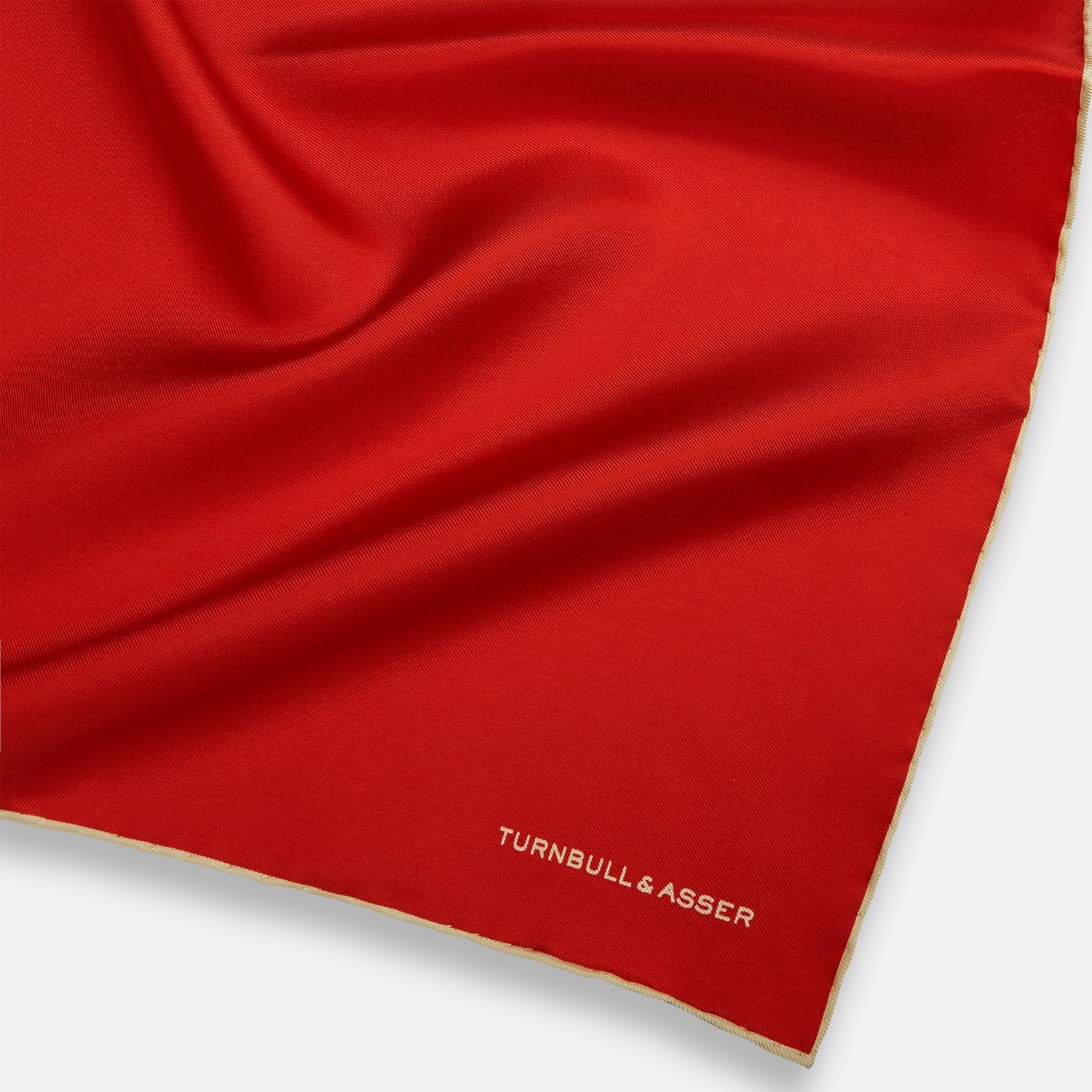 View 2 of product The Turnbull & Asser RED AND GOLD PIPED SILK POCKET SQUARE is a vibrant red silk accessory with gold edging and the brand’s logo in white on the bottom right—ideal for elevating formal looks.