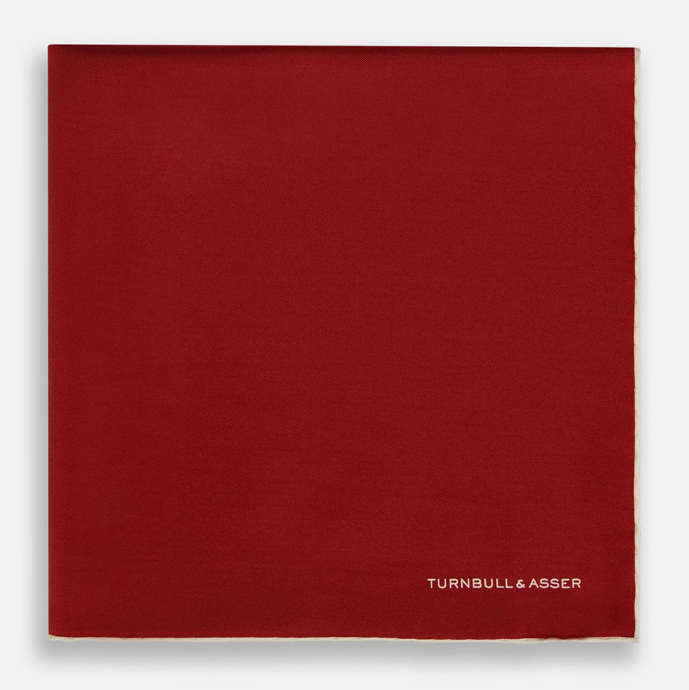 The Turnbull & Asser Burgundy and Ecru Piped Silk Pocket Square features a classic square design, contrasting ecru piping on the edge, and white branding in the lower corner—a refined accessory for formal looks.
