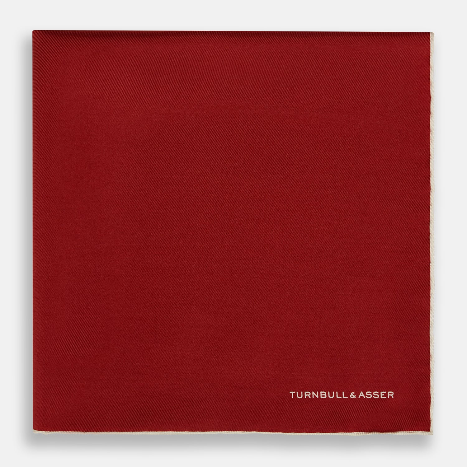 View 3 of product The Turnbull & Asser Burgundy and Ecru Piped Silk Pocket Square features a classic square design, contrasting ecru piping on the edge, and white branding in the lower corner—a refined accessory for formal looks.