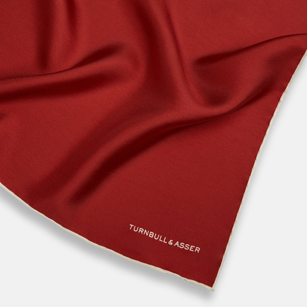 The Turnbull & Asser Burgundy and Ecru Piped Silk Pocket Square features a classic square design, contrasting ecru piping on the edge, and white branding in the lower corner—a refined accessory for formal looks.