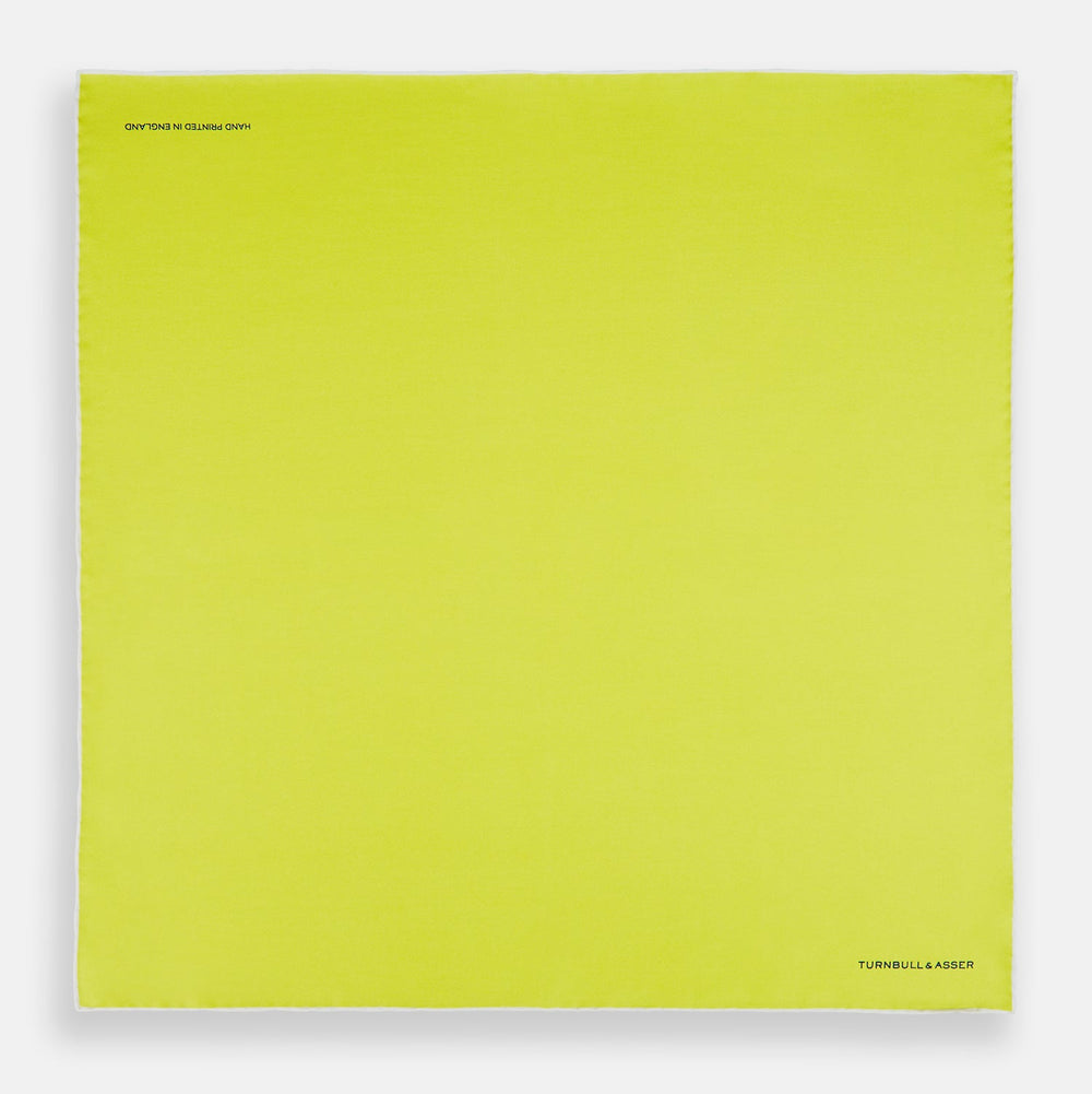 The Canary Yellow Piped Silk Pocket Square by Turnbull & Asser features white edges and black branding in the bottom right corner, making it a perfect accessory for formal attire. Shown on a plain white background.