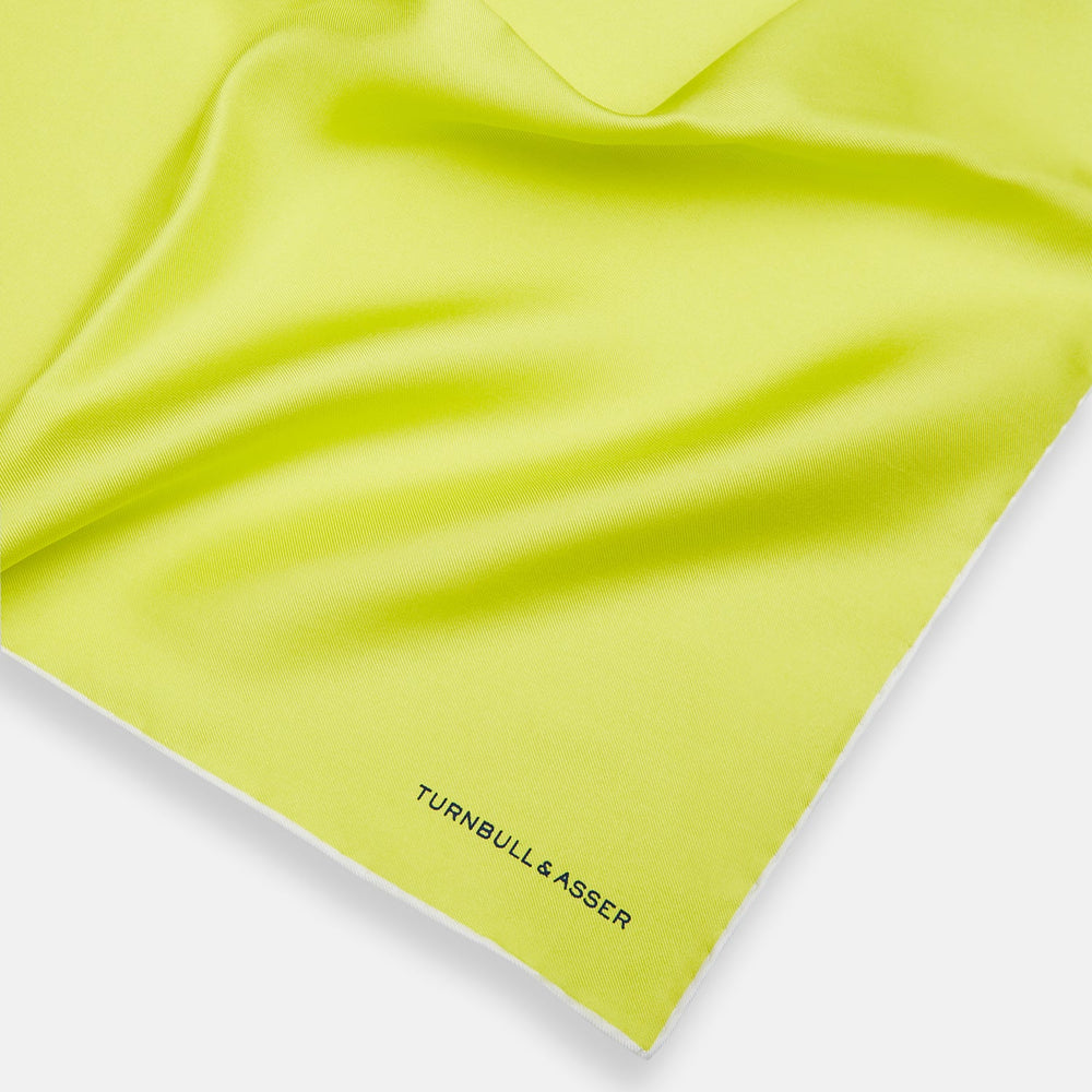 The Canary Yellow Piped Silk Pocket Square by Turnbull & Asser features white edges and black branding in the bottom right corner, making it a perfect accessory for formal attire. Shown on a plain white background.